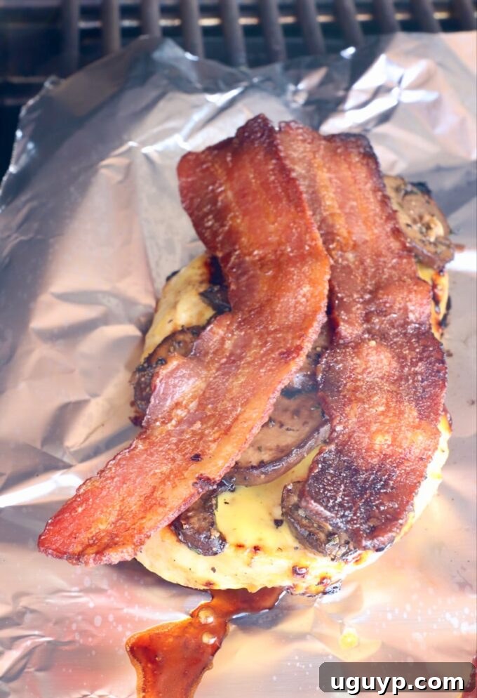 Grilled chicken adorned with slices of crispy bacon, placed on foil on the grill.