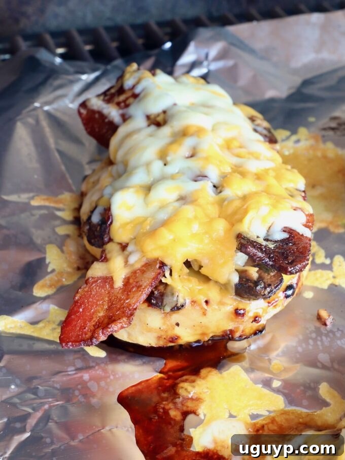 Irresistible grilled chicken, generously topped with crispy bacon and perfectly melted cheese, showcased on foil within a grill.