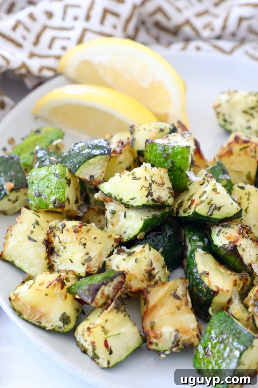 Seasoned cooked diced zucchini on a plate with lemon wedges, ready to serve