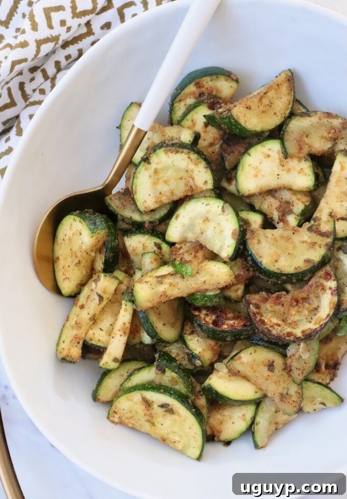Cooked sliced zucchini in a bowl with a serving spoon