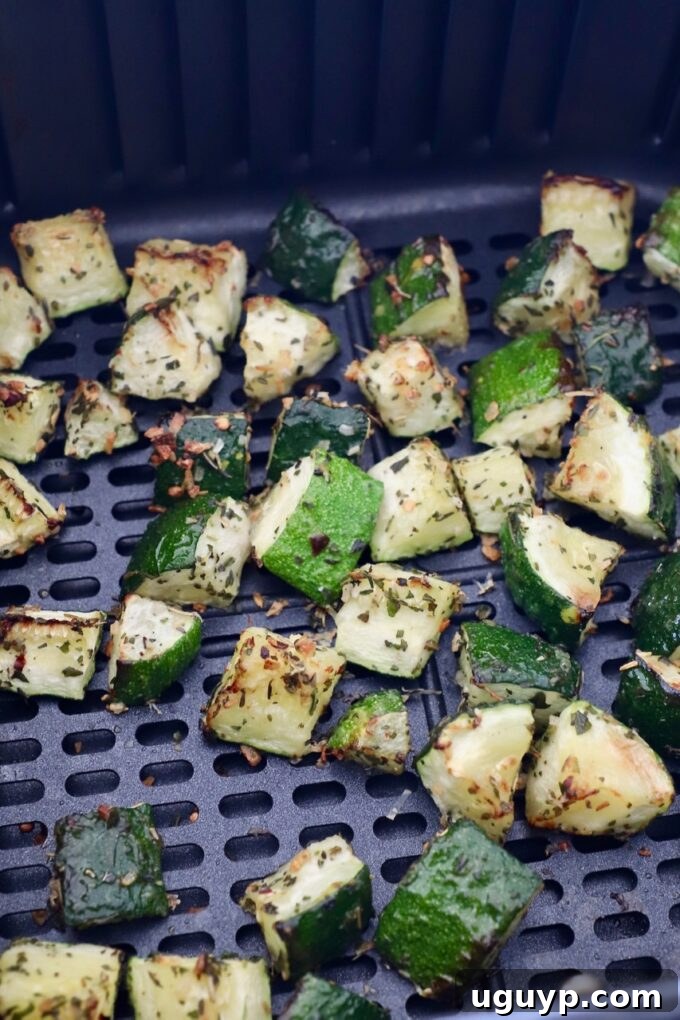 Cooked diced zucchini in an air fryer basket, showing crispy edges