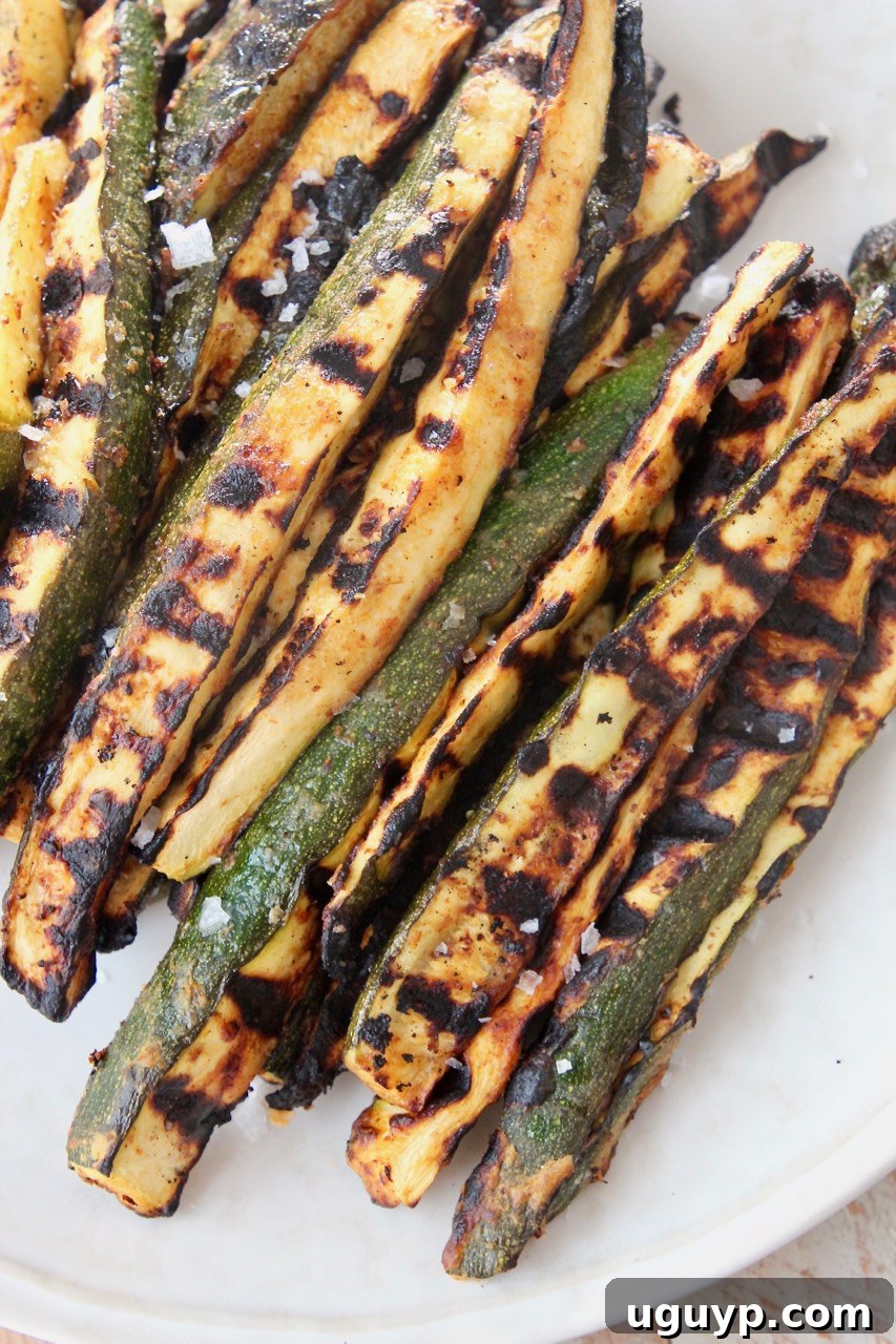 Grilled zucchini spears on a plate, garnished with fresh herbs