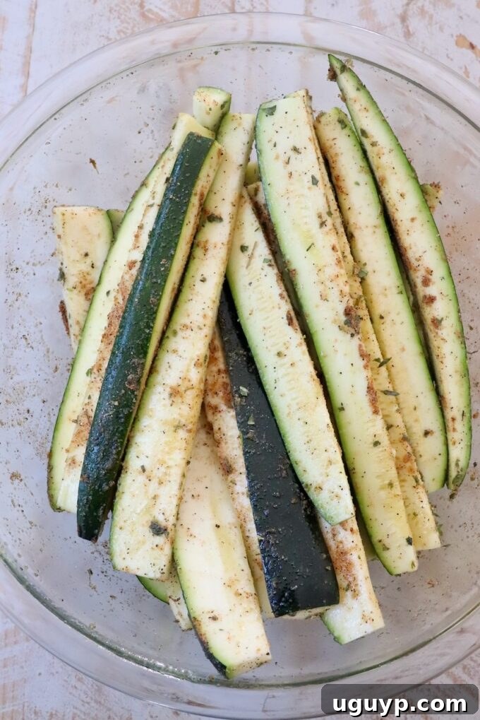 Seasoned zucchini spears in a large glass bowl, ready for grilling