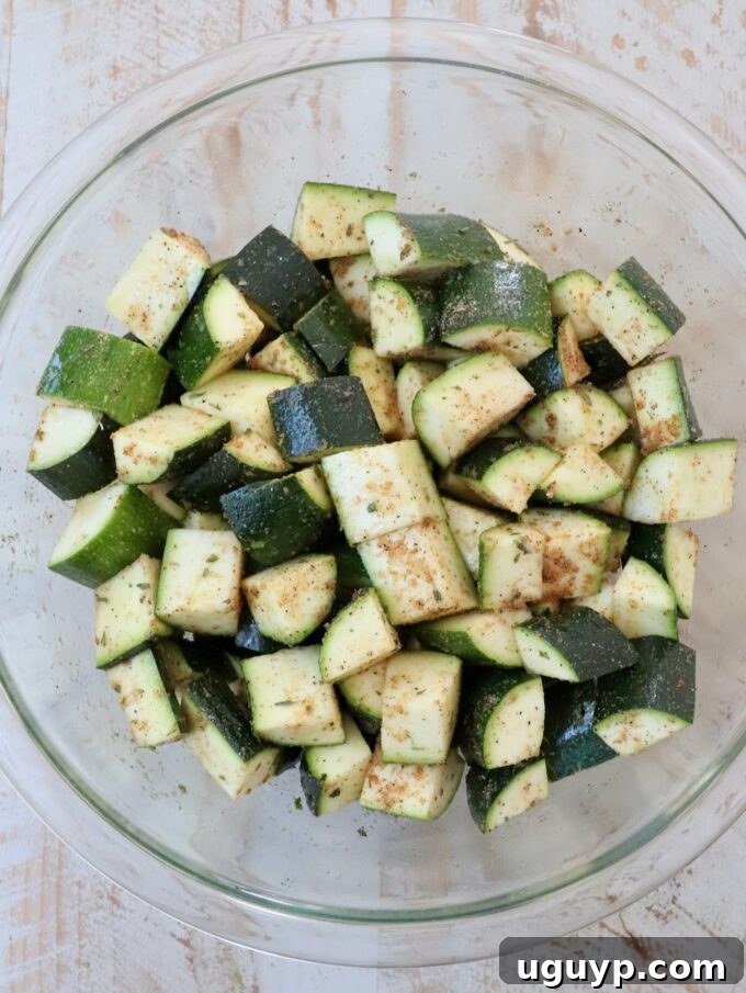 Seasoned diced zucchini in a glass bowl, ready for oven roasting