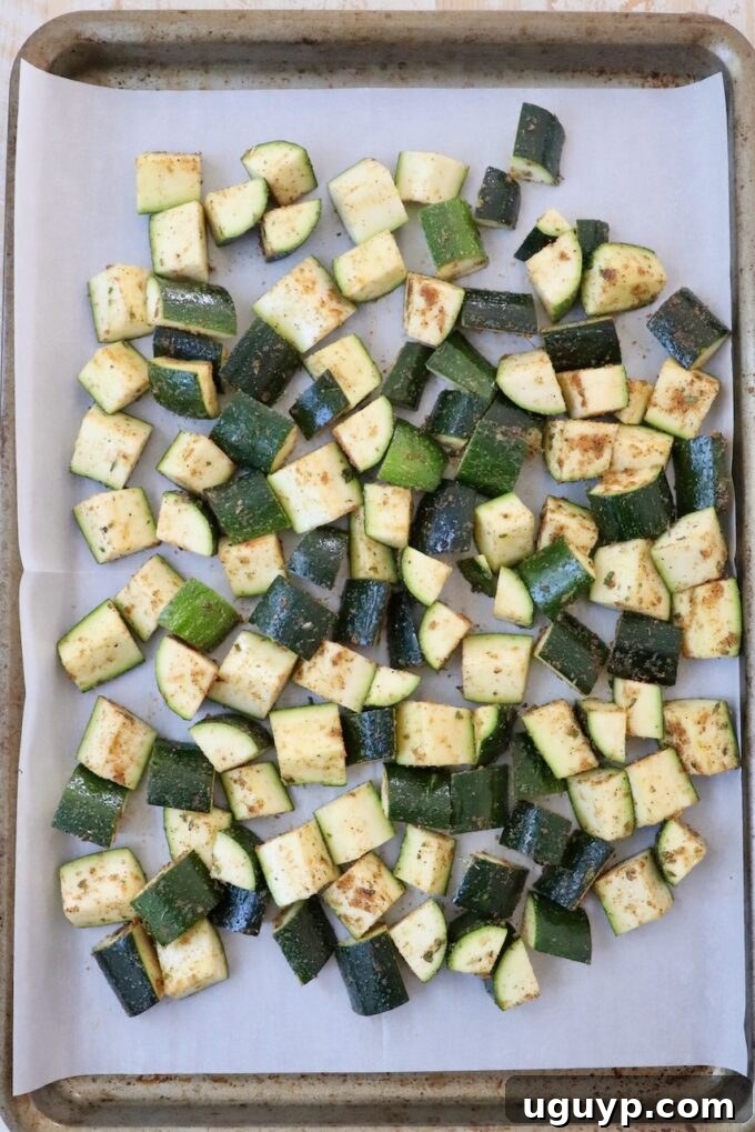 Seasoned diced zucchini spread evenly on a parchment-lined baking sheet