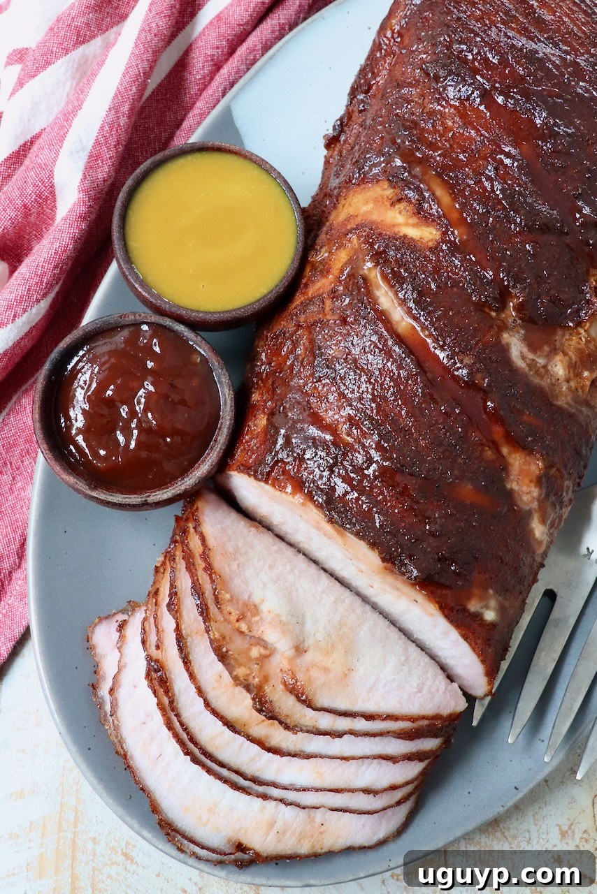 partially sliced smoked pork loin on plate with two sides of bbq sauce