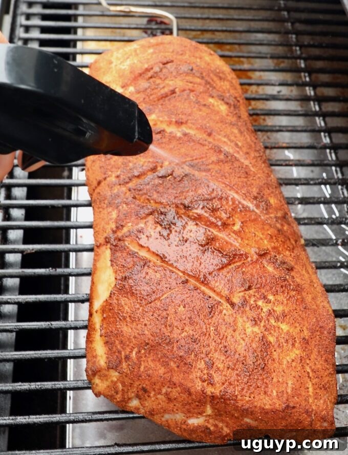 Seasoned pork loin on the smoker, being gently spritzed with apple juice to maintain moisture, enhance flavor, and perfect the bark.