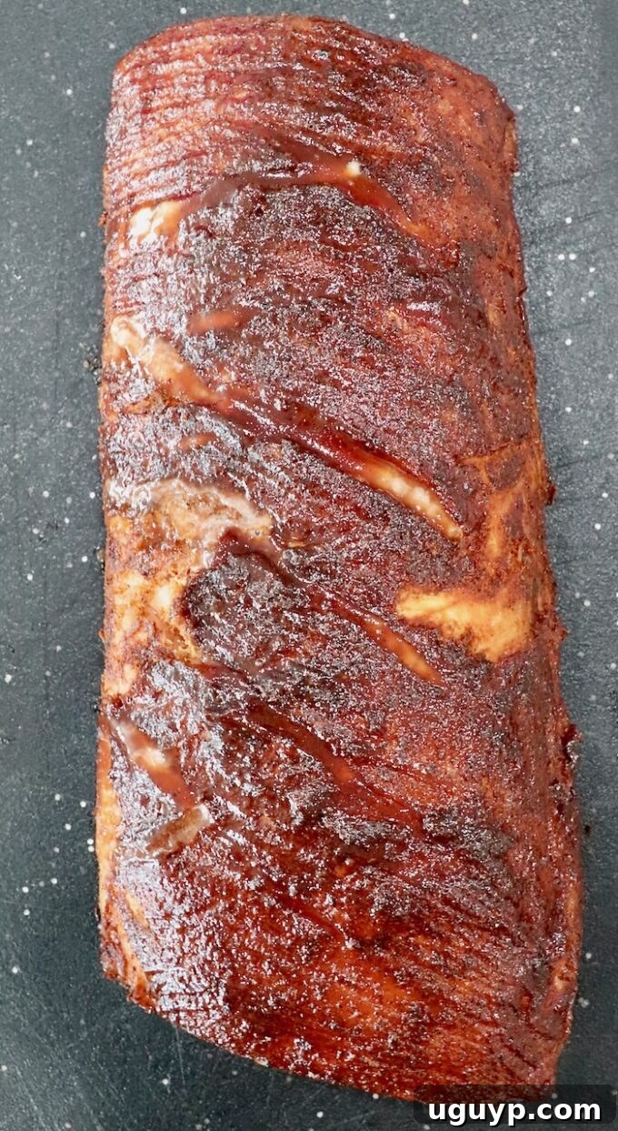 A perfectly glazed smoked pork loin, removed from the smoker and resting on a cutting board, ready for the crucial resting period before slicing.