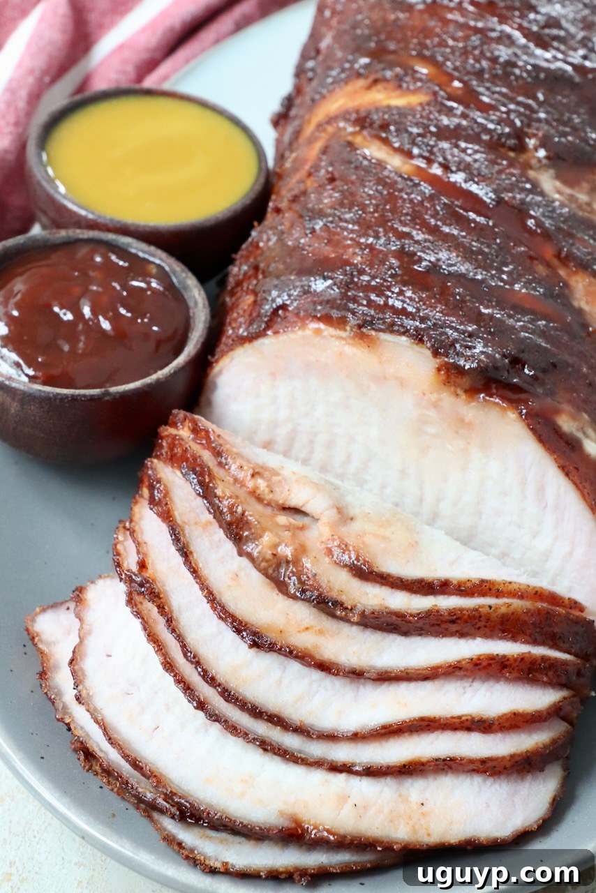 Perfectly smoked and thinly sliced pork loin displayed on a plate, accompanied by two small bowls of delicious BBQ sauce for dipping and enhancing the flavor.