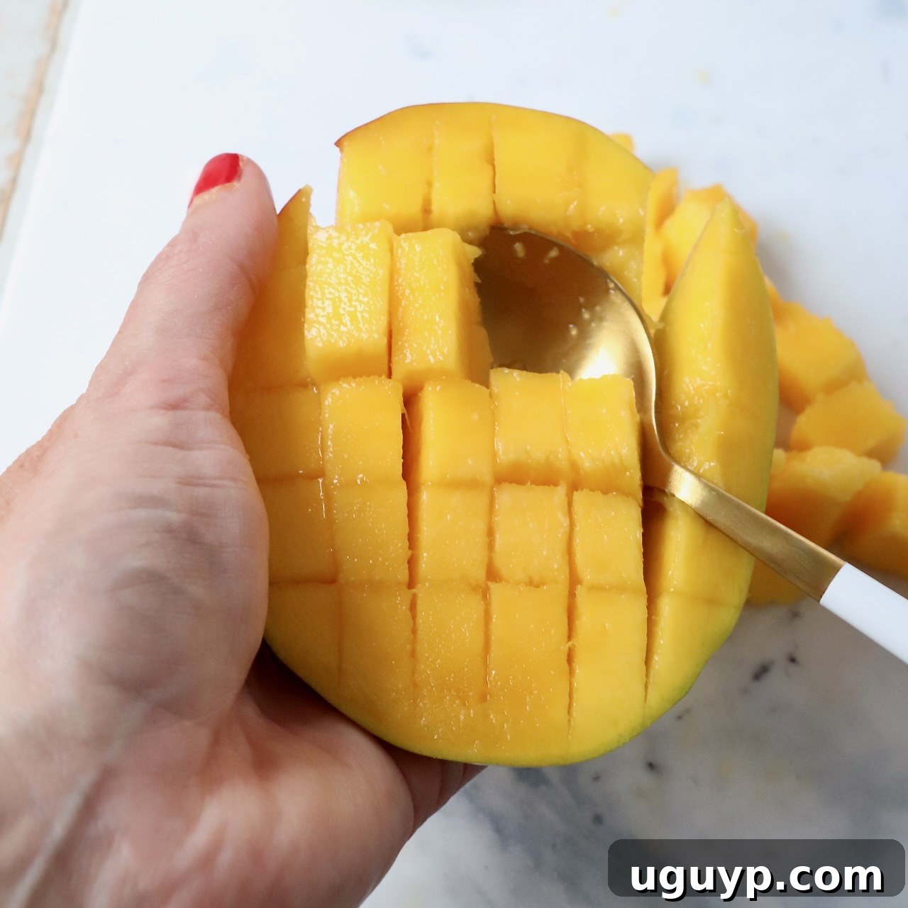 Freshly cut mango cubes displayed elegantly within the mango skin, with a spoon resting beside it, highlighting its readiness for consumption.