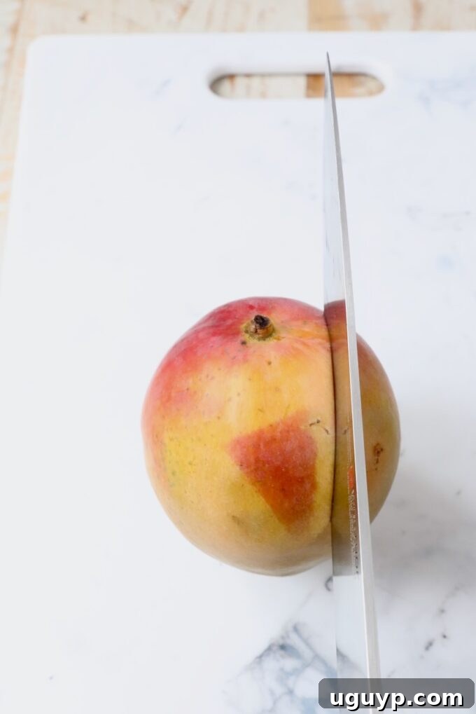 A sharp knife carefully slicing through the side of a vibrant mango, preparing to separate the flesh from the central seed.