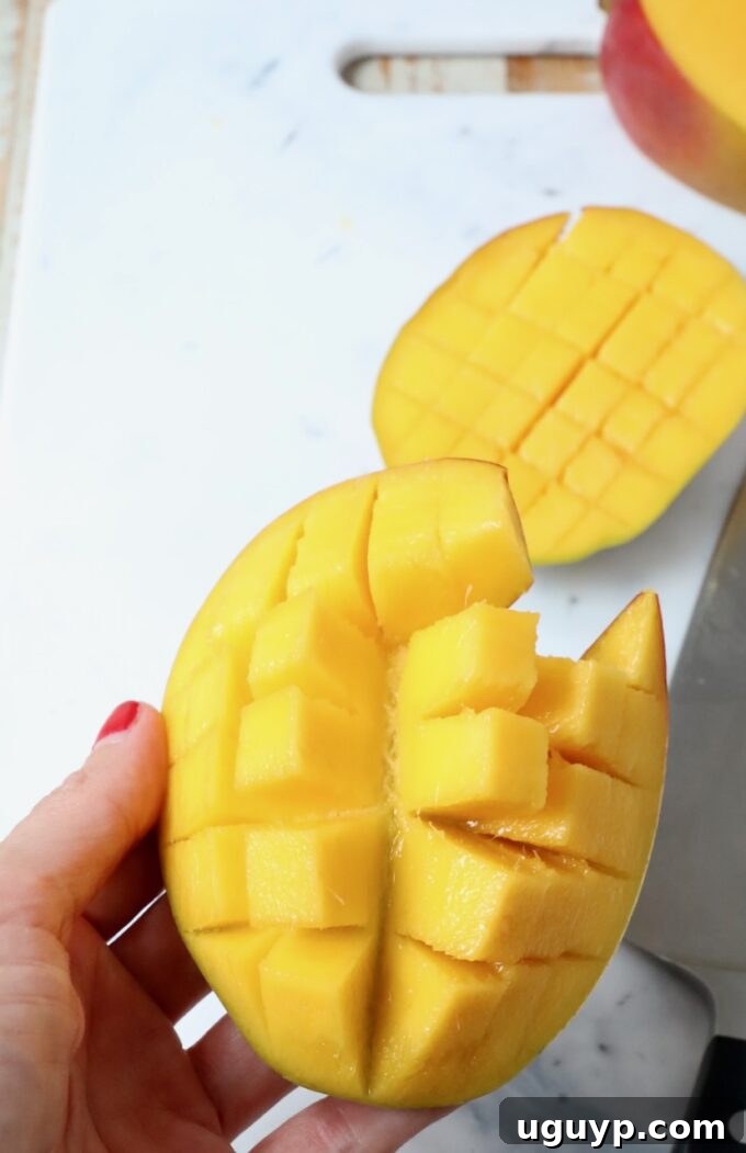 A hand expertly holding a scored mango cheek over a cutting board, poised for the next step of flesh removal.