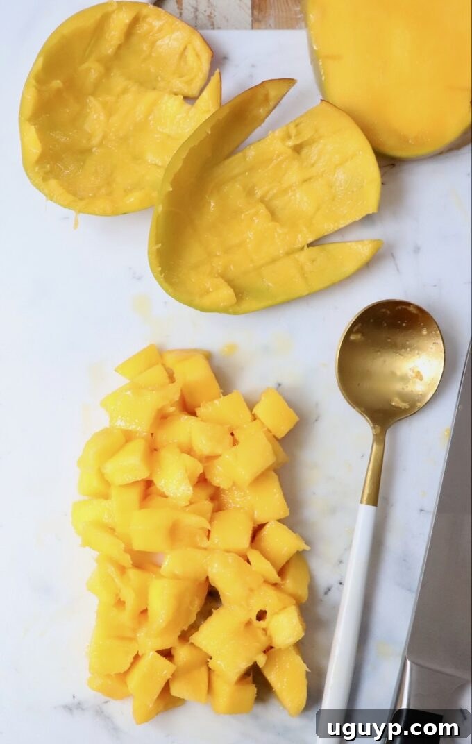 A pile of fresh, vibrant diced mango on a cutting board, accompanied by a spoon, showcasing the delicious end result.
