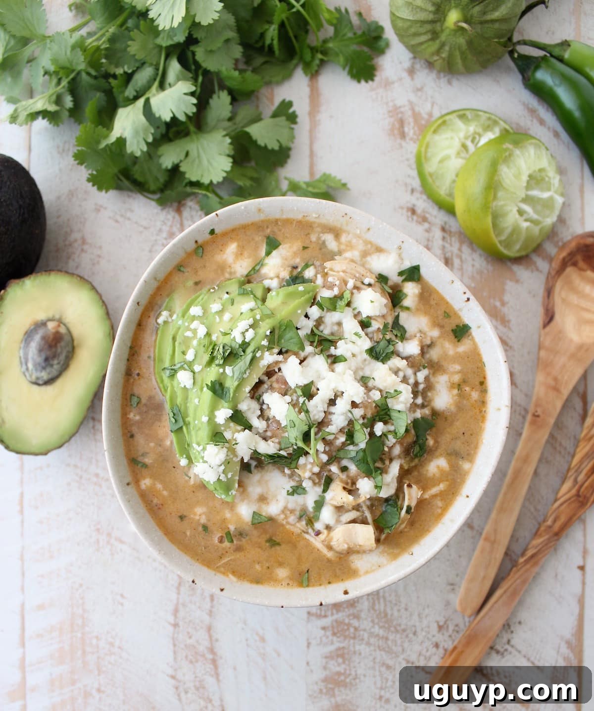 Green Chili Chicken Enchilada Soup topped with creamy avocado slices, fresh cilantro, and a sprinkle of cheese on a rustic wooden surface, ready to be enjoyed.