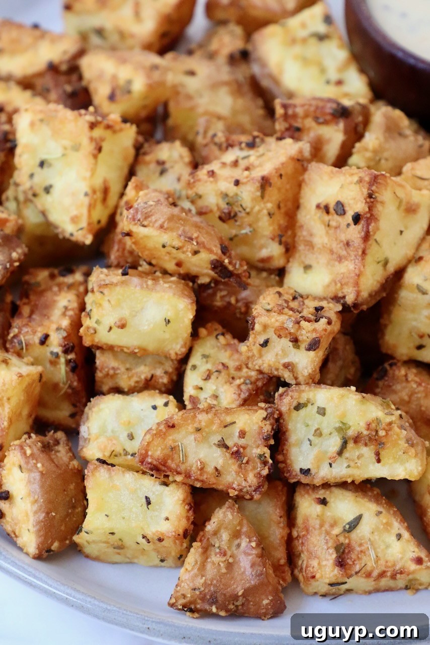 Golden brown, crispy cubed roasted potatoes served on a white plate, garnished lightly with herbs.