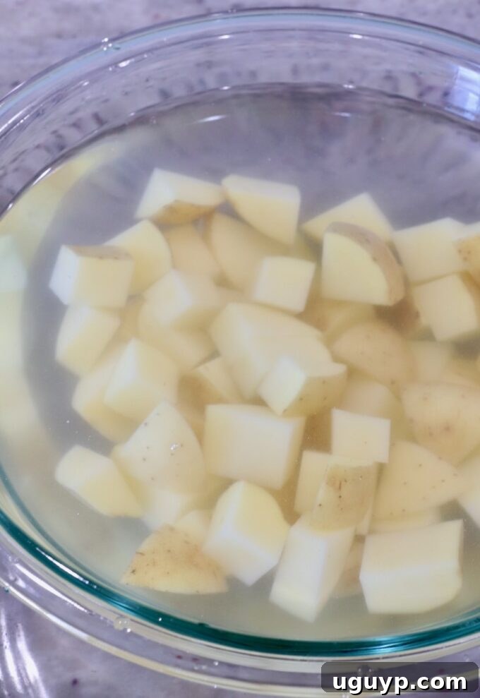 Cubed potatoes submerged in a bowl of salted water, illustrating the optional soaking step for extra crispiness.