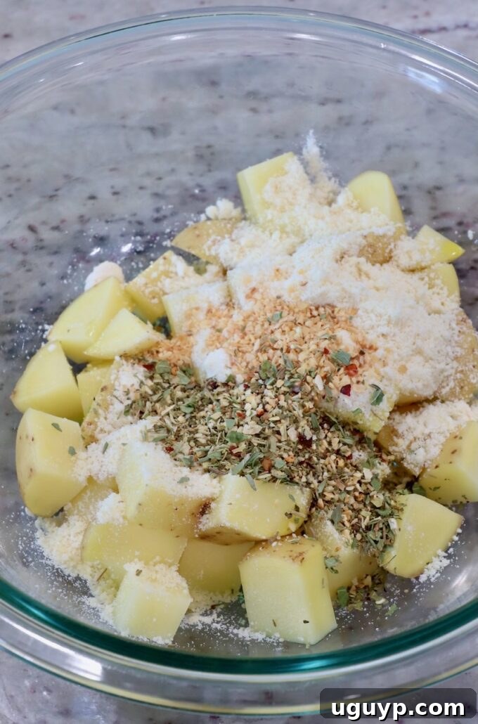 Cubed potatoes, olive oil, parmesan cheese, Italian seasoning, sea salt, and dried minced garlic in a glass bowl, ready to be tossed.