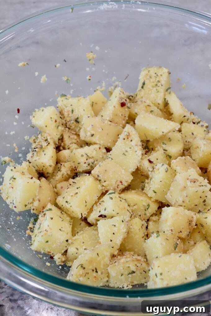 Seasoned and coated potato cubes in a glass bowl, perfectly mixed with the oil, cheese, and spices.