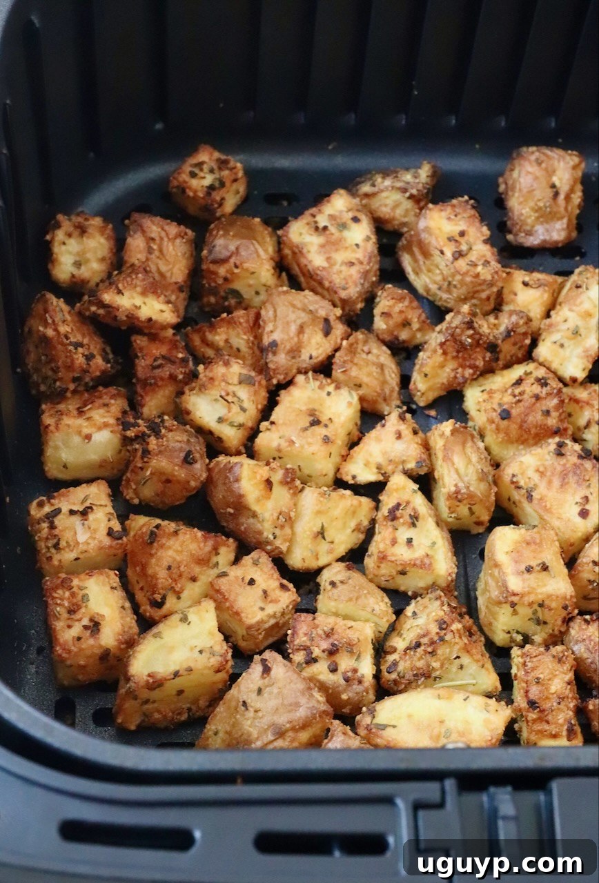 Perfectly roasted, golden-brown potato cubes piled high in an air fryer basket, showing off their crispy exterior.