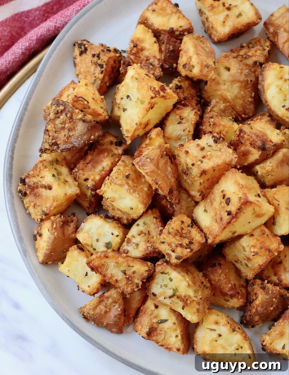 Close-up of crispy, golden air fryer roasted potatoes with herbs on a white plate, highlighting their textured surface.