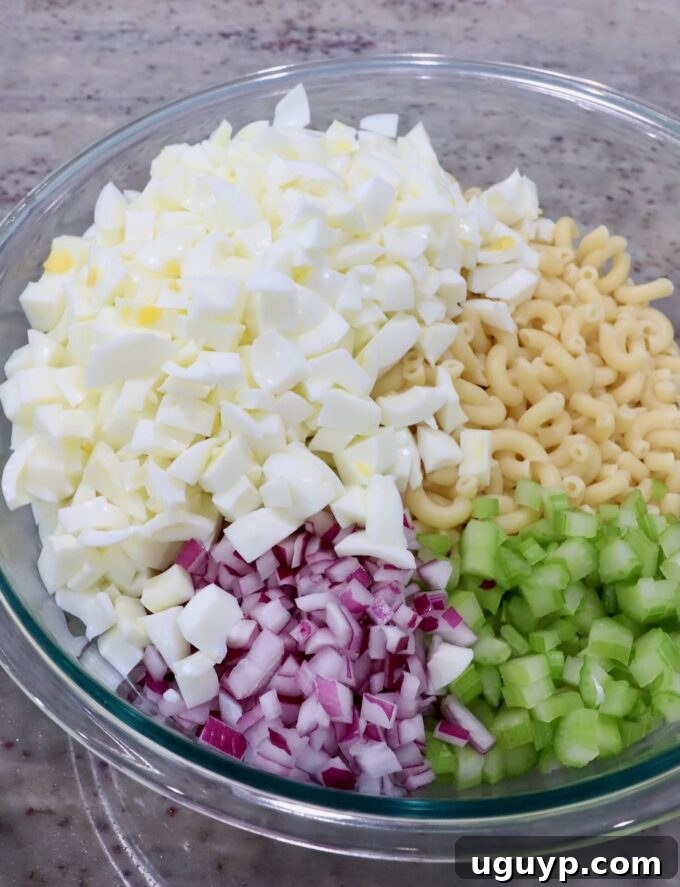 diced egg whites in a large glass bowl with cooked macaroni noodles, diced onions and diced celery