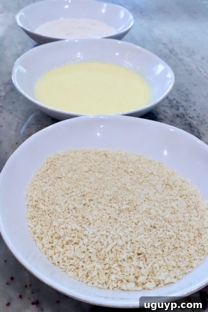 three bowls lined up, one filled with breadcrumbs, one with flour and another with buttermilk