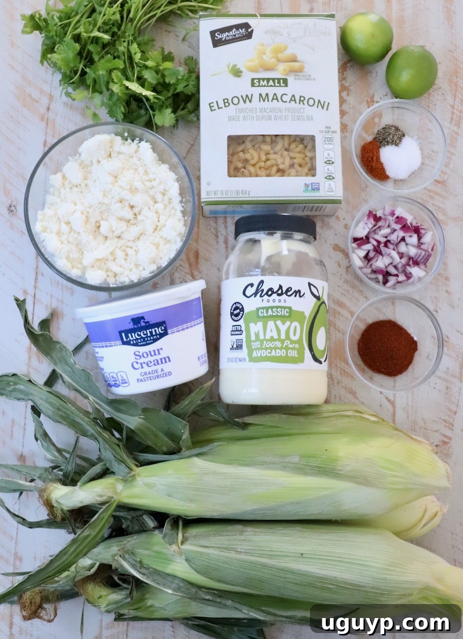 Fresh ingredients for Mexican street corn pasta salad, including corn, red onion, cilantro, and cotija cheese on a white wooden board.