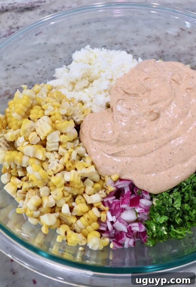 Mexican street corn pasta salad ingredients being tossed with the creamy dressing in a large glass bowl.