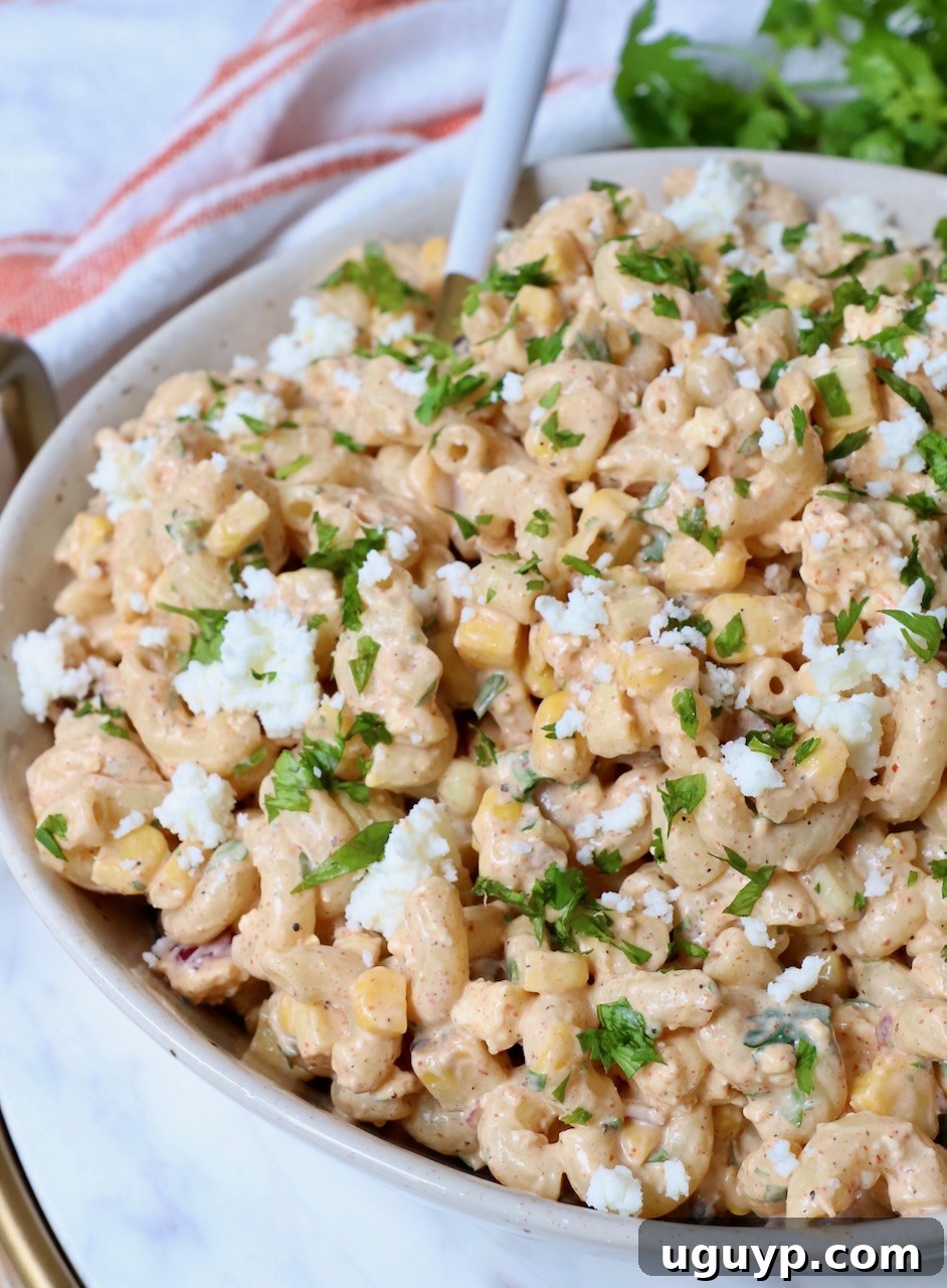Close-up of Mexican street corn pasta salad in a bowl with a serving spoon, showing creamy texture and colorful ingredients.