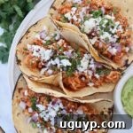 tacos on plate filled with cooked, shredded chicken, cheese, diced onions and cilantro