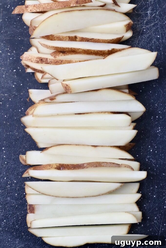 potatoes sliced into french fries on cutting board