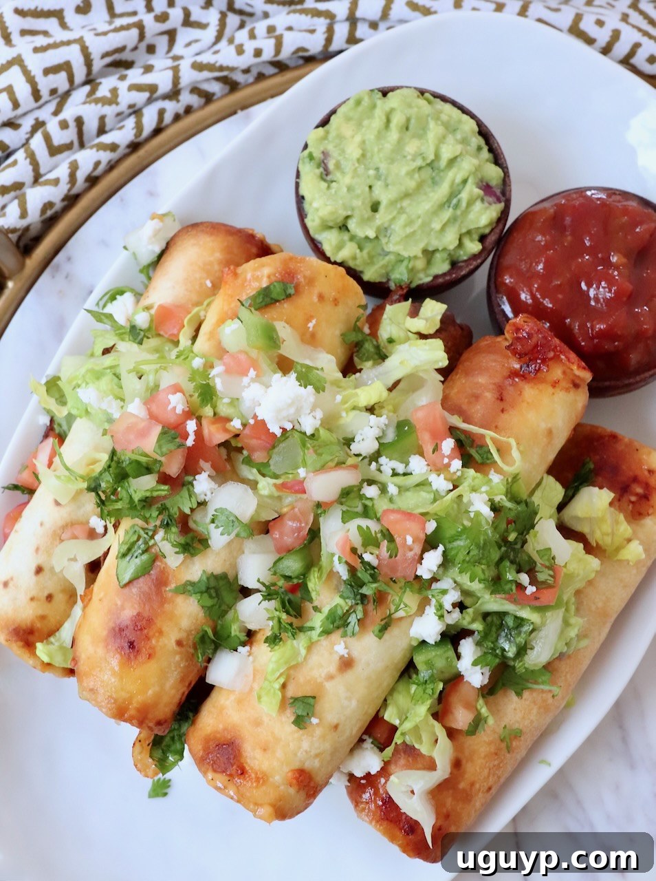 Crispy beef taquitos stacked on a plate, generously topped with fresh guacamole and vibrant pico de gallo, ready to be enjoyed.
