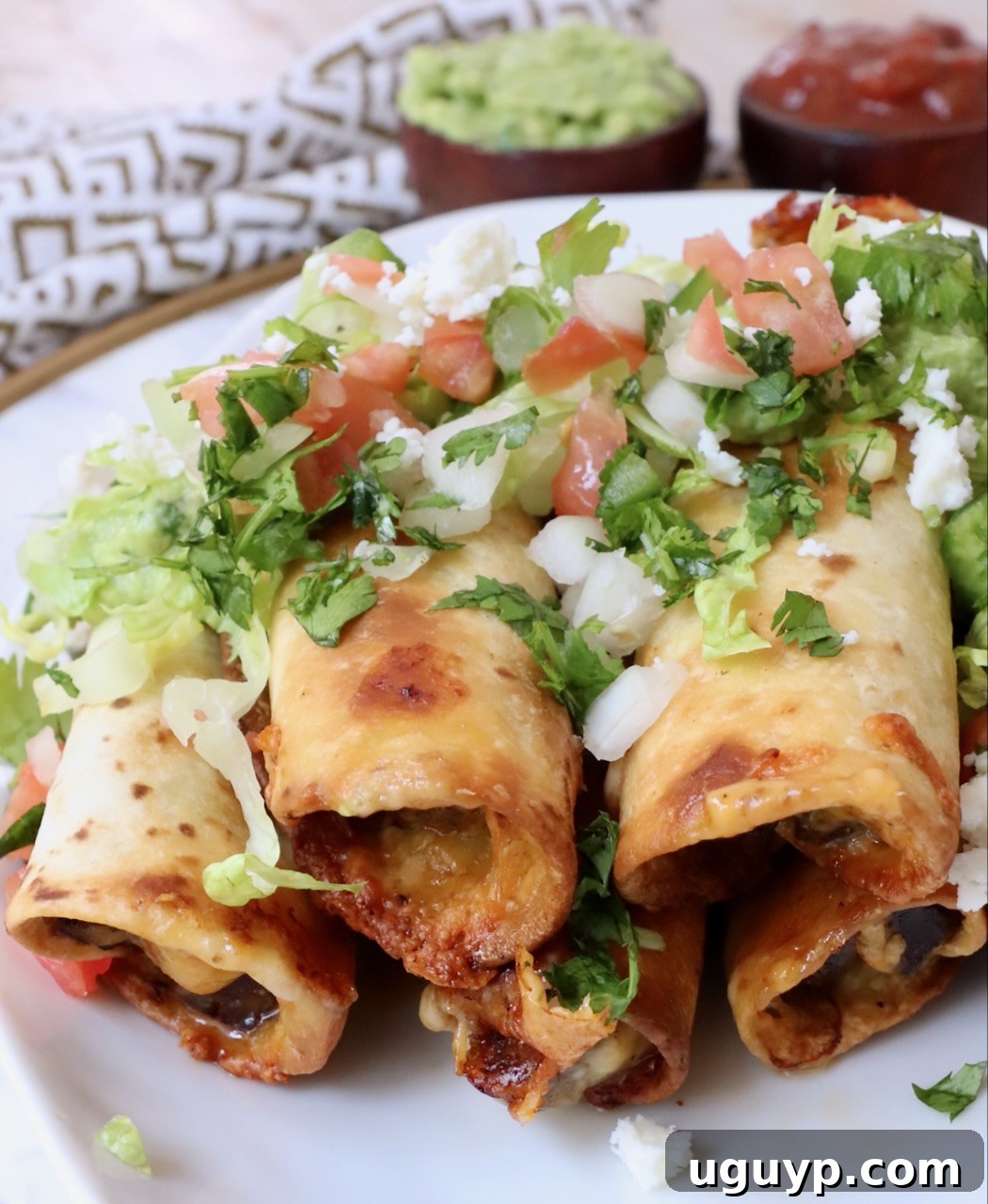 A stack of perfectly cooked beef taquitos on a plate, topped with fresh pico de gallo, showcasing their golden crispness.