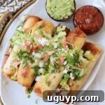 Golden brown beef taquitos stacked on a plate, topped with a generous amount of fresh guacamole, pico de gallo, and cilantro.
