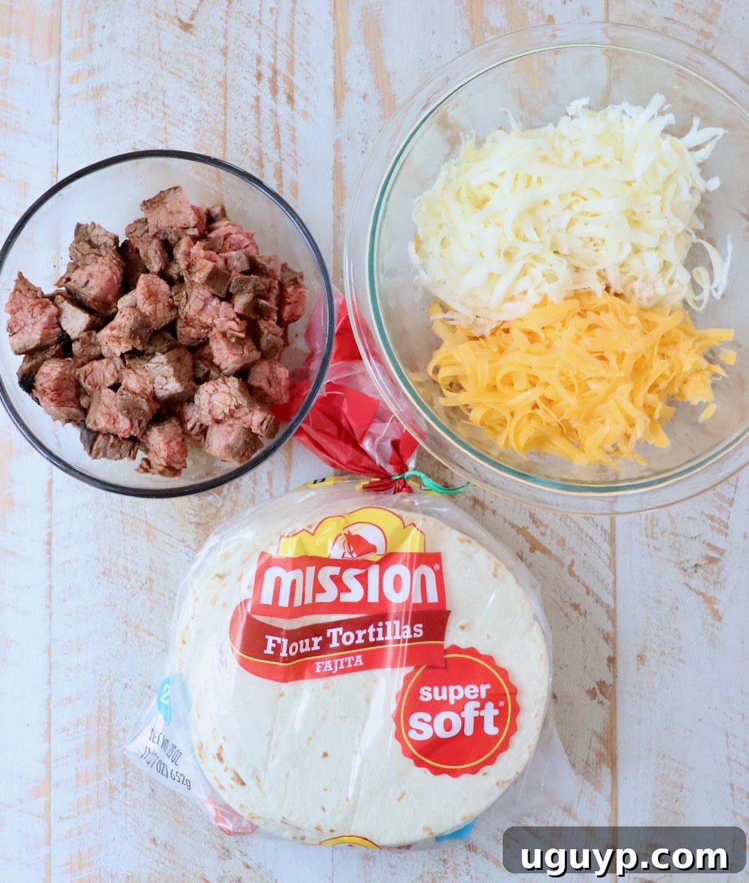 All the ingredients for beef taquitos neatly arranged on a white wooden board, including seasoned steak, shredded cheese, and tortillas.