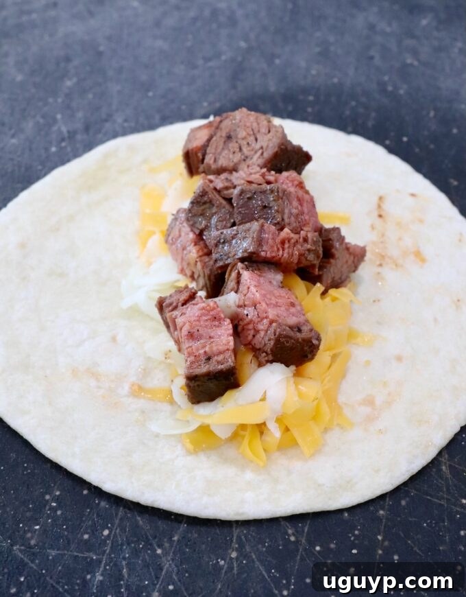 A flour tortilla laid flat on a cutting board, topped with shredded cheese and small diced pieces of grilled carne asada, ready to be rolled.
