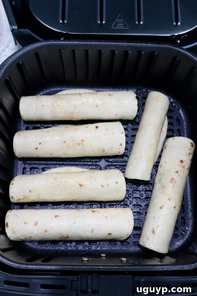 Uncooked beef taquitos arranged neatly, seam-side down, in the basket of an air fryer, ready for cooking.