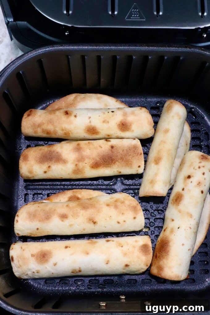 Golden brown and perfectly crispy cooked beef taquitos resting in the air fryer basket after cooking.