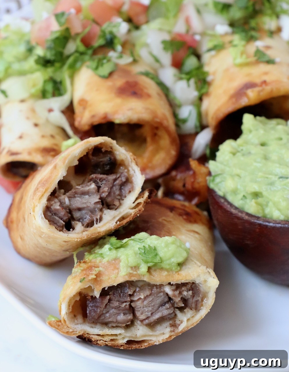 A perfectly cooked steak taquito, cut in half to reveal the cheesy carne asada filling, served alongside fresh guacamole on a plate.