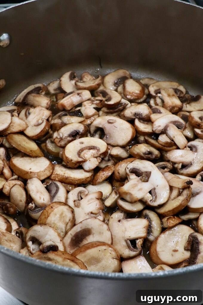 Sliced mushrooms being added to a large pot with melted butter and oil, ready for sautéing.