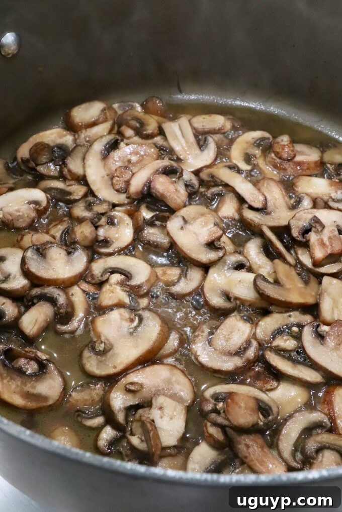 Sautéed sliced mushrooms simmering in vegetable broth in a large pot, reducing for maximum flavor.