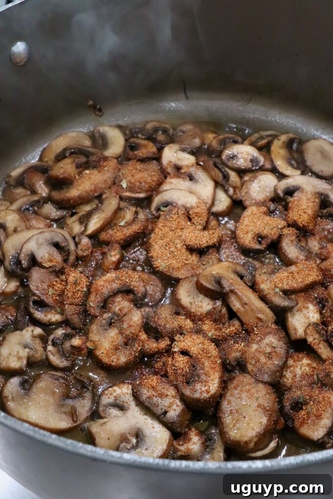 Cooked sliced mushrooms being seasoned with taco seasoning in a large pot, ensuring even coating.