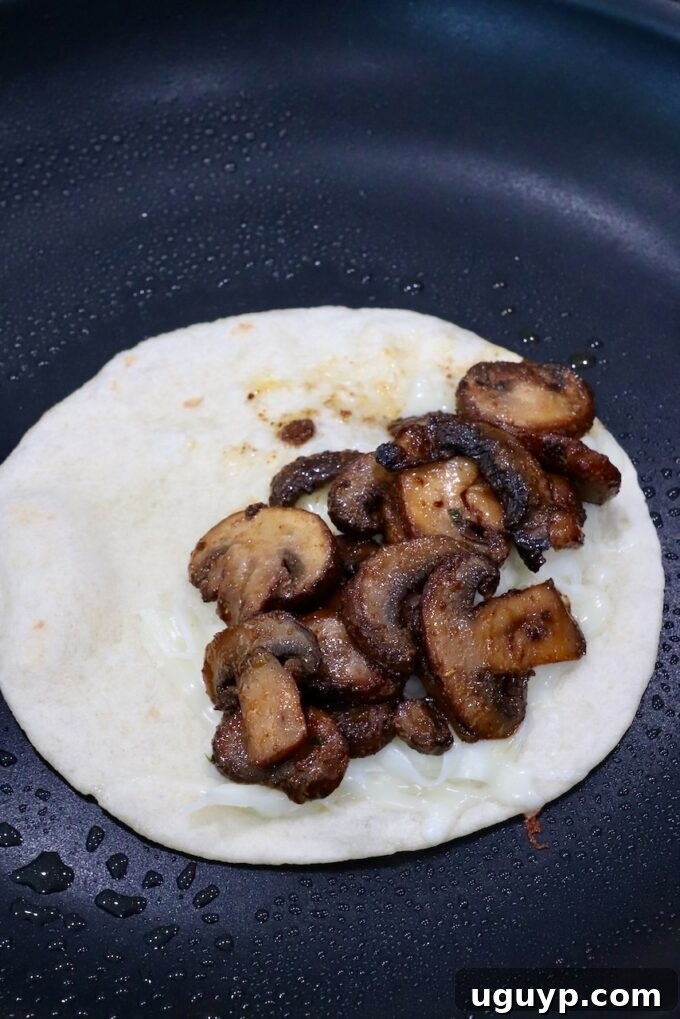 A generous portion of sautéed mushrooms placed over melted cheese on a tortilla in a skillet, ready for folding.