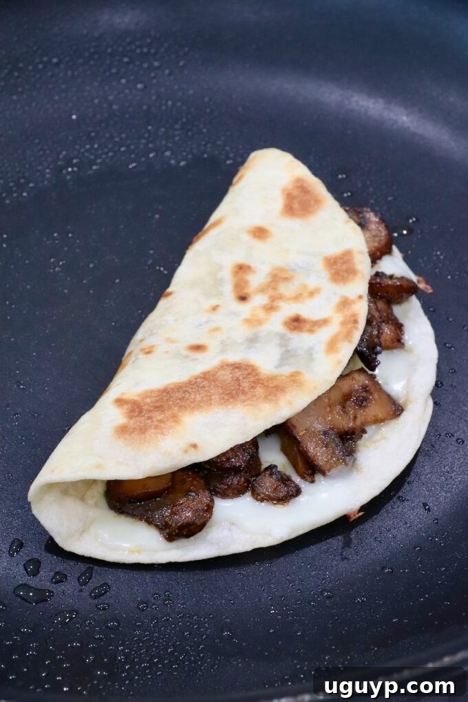 A mushroom taco folded in a skillet, with cheese oozing out, achieving a perfect crispy exterior.