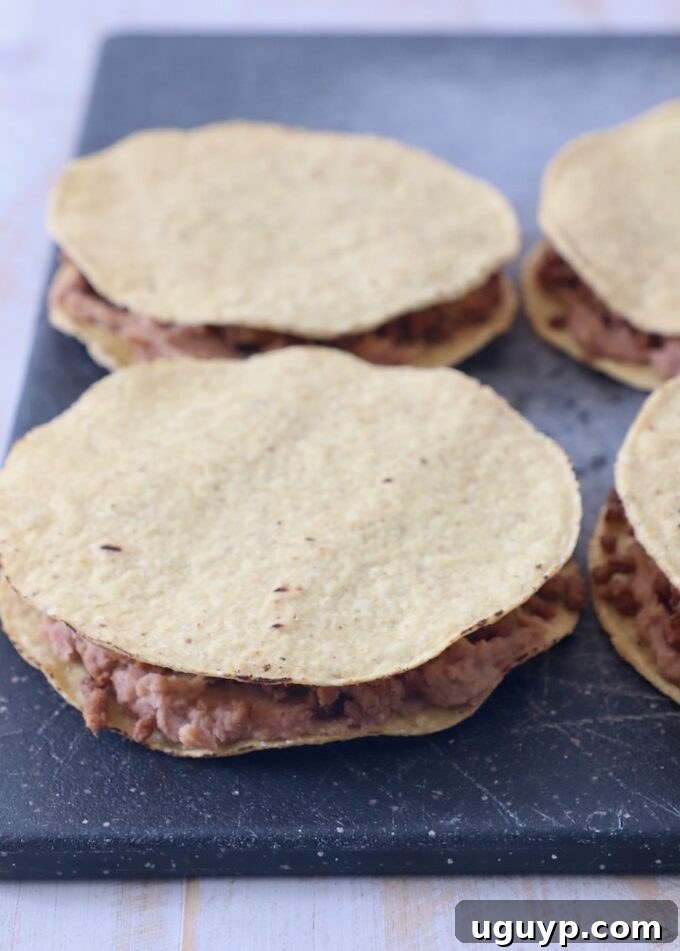 ground beef and refried beans sandwiched between tostada shells on a cutting board