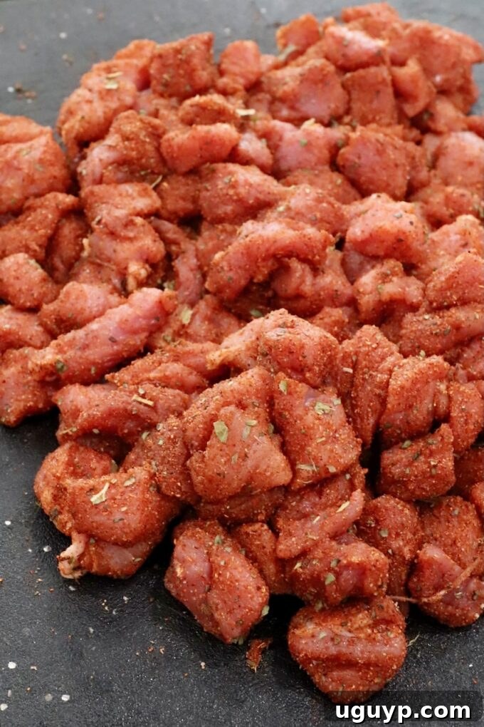 Diced and seasoned pork tenderloin pieces on a cutting board, ready for cooking.
