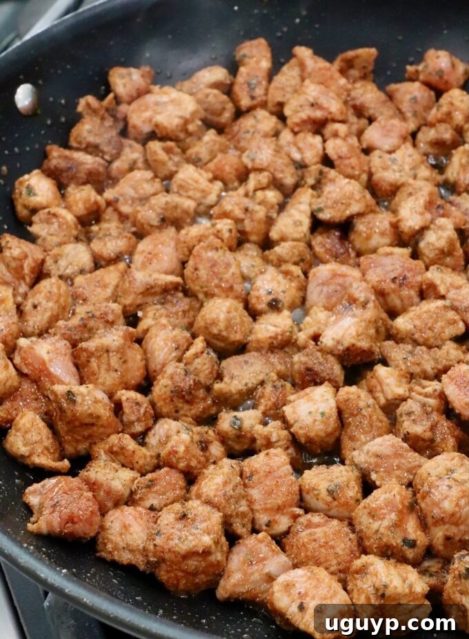 Seasoned, diced pork cooking in a hot skillet, browning beautifully.