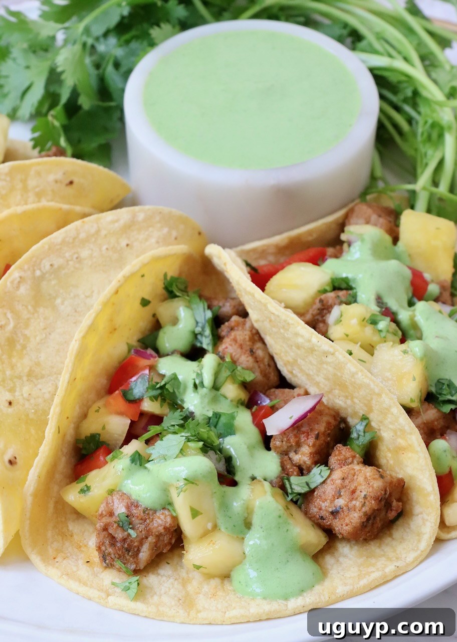 Close-up of pork tacos drizzled with cilantro lime sauce, served on a plate.