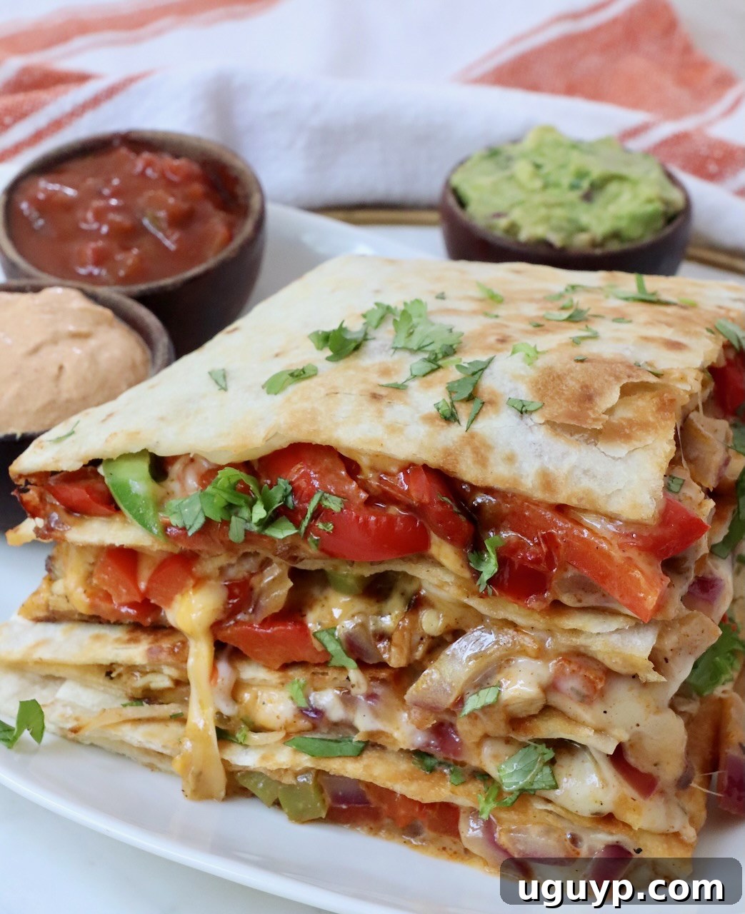 Two halves of a perfectly cooked chicken quesadilla, stacked one on top of the other, revealing layers of melted cheese, tender chicken, and colorful fajita vegetables.