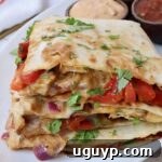 Perfectly sliced chicken quesadilla quarters stacked on a plate, ready to be served, showcasing its golden tortilla and savory filling.